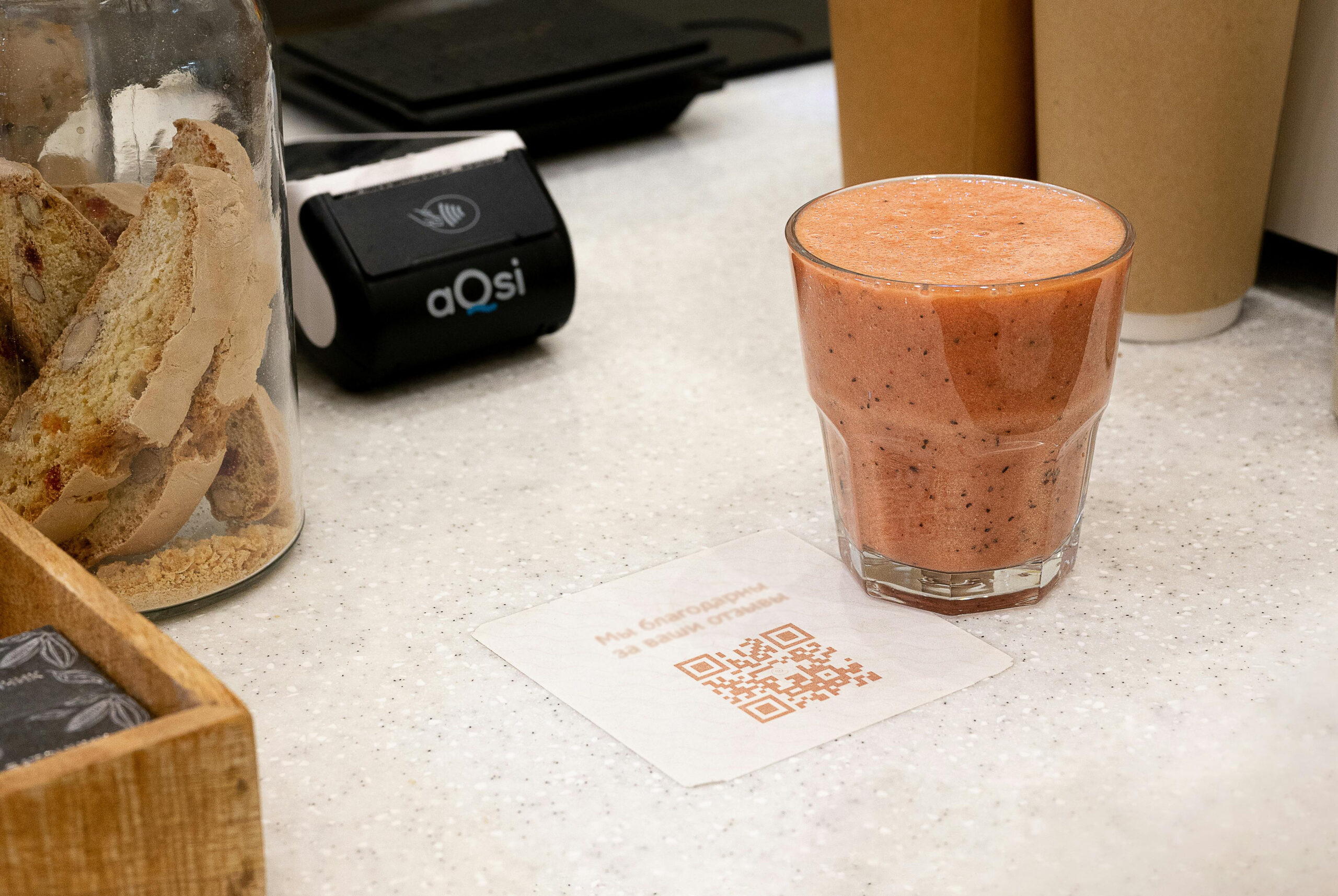 Front counter of a food service retail location with a pink drink in a glass beside a QR code.